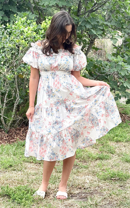 Model wearing a romantic floral off-shoulder midi dress with tiered skirt and puff sleeves, styled for a summer celebration