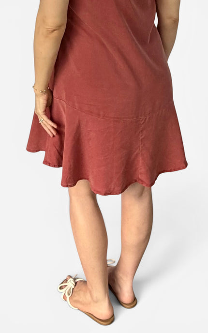 A person wearing a dusty rose or terracotta-colored sleeveless dress, shown from the back with their legs and feet visible, wearing beige flat sandals against a light gray background.
