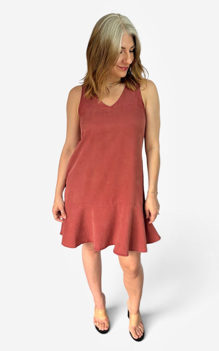 A woman modeling a sleeveless V-neck shift dress in a dusty rose color, paired with black flat sandals, against a plain white studio background.