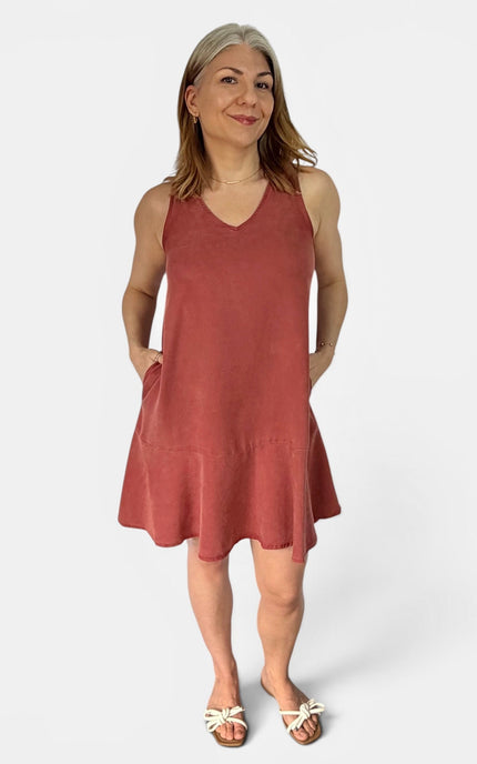 A woman modeling a sleeveless, tiered V-neck dress in a dusty rose color, paired with white slide sandals, against a plain light gray background.