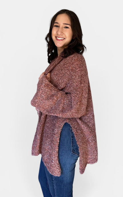 A woman modeling a loose, long-sleeve knit poncho or cardigan in a heathered dusty rose and burgundy color, paired with blue jeans, against a plain light gray background.