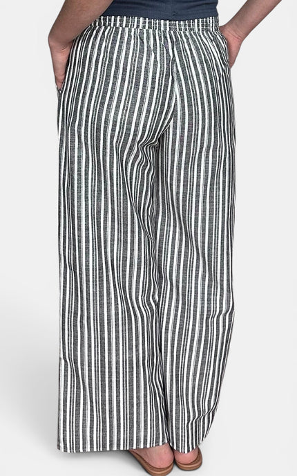 A person wearing wide-leg pants with vertical black and white stripes, shown from the waist down against a light gray studio background.