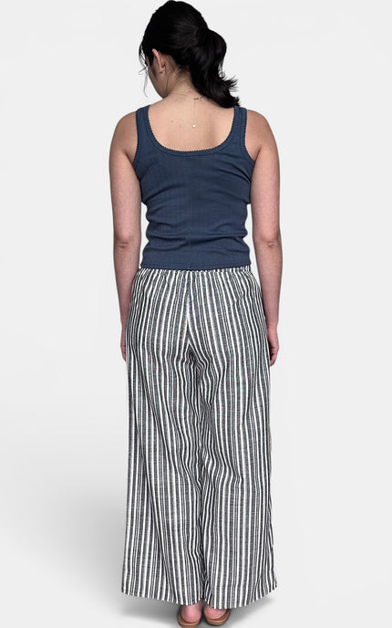 A woman modeling a navy blue sleeveless top and black and white vertically striped wide-leg pants against a light gray studio 