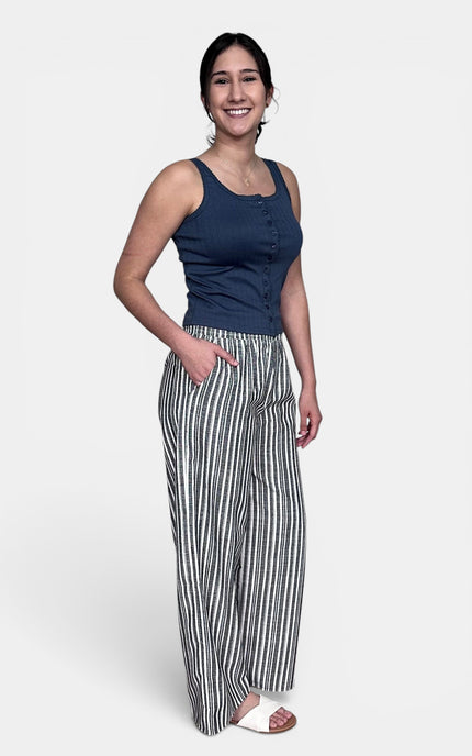 A woman modeling a navy blue sleeveless top and black and white vertically striped wide-leg pants against a light gray studio background.