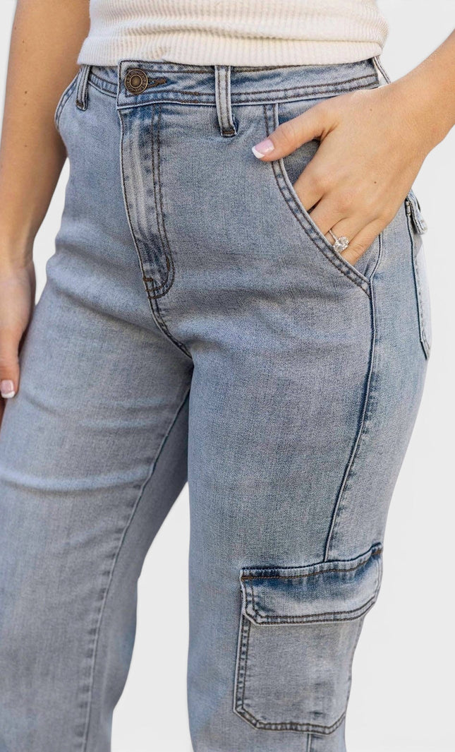 Close-up of a person wearing light blue denim cargo jeans with a cream ribbed top, showing the front and side pockets against a plain light background.