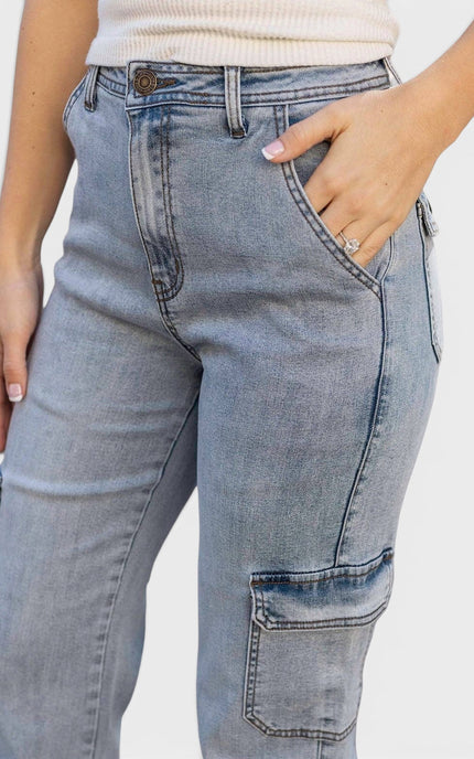 Close-up of a person wearing light blue denim cargo jeans with a cream ribbed top, showing the front and side pockets against a plain light background.
