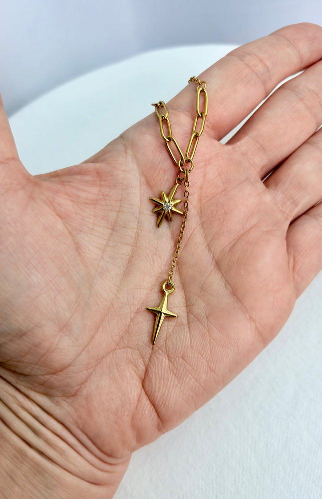 Close‑up of star, cross, and tassel pendants cradled in a hand, highlighting detail and shine.