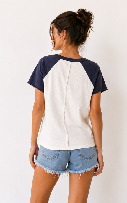 Person wearing a navy and white baseball-style shirt with denim shorts on a plain background