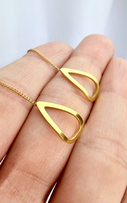 A close-up photo of the gold triangle threader earrings resting in an open palm, with the delicate 6cm chains gracefully spilling over the side of the hand to showcase their fluid movement and polished 18k gold shine.