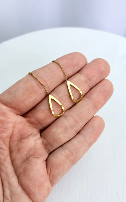 A minimal, handheld shot of a pair of gold geometric threader earrings in a palm. The tight crop focuses on the clean, architectural lines of the open triangle charms and the high-quality, tarnish-free gold finish.