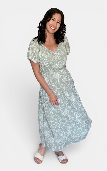 Light sage green midi dress with a white floral pattern, featuring short puff sleeves and a V-neckline, set against a plain light gray background.