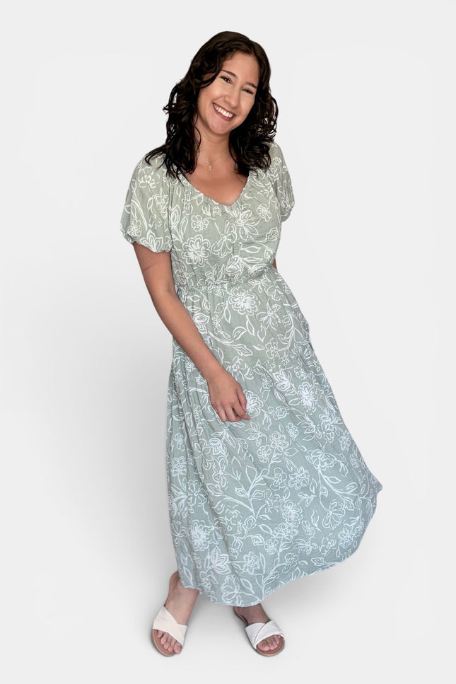 Light sage green midi dress with a white floral pattern, featuring short puff sleeves and a V-neckline, set against a plain light gray background.