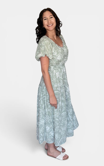 Light sage green midi dress with a white floral pattern, featuring short puff sleeves and a V-neckline, set against a plain light gray background.