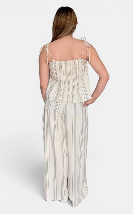 A woman shown from the back wearing a sleeveless striped jumpsuit with tie shoulder straps and wide-leg pants, photographed against a light gray studio background.