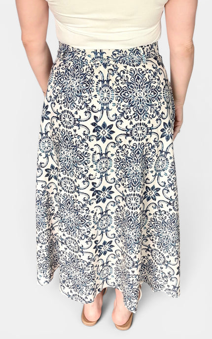 A woman wearing a high-waisted, midi-length A-line skirt with a navy blue and cream floral damask pattern, paired with a cream top and beige heels.