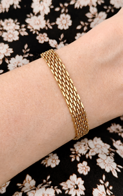 A close-up of a gold multi-strand chain bracelet worn on a person's wrist, set against a black and white floral patterned fabric background.