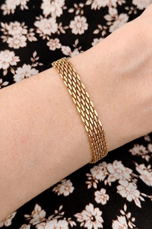 A close-up of a gold multi-strand chain bracelet worn on a person's wrist, set against a black and white floral patterned fabric background.