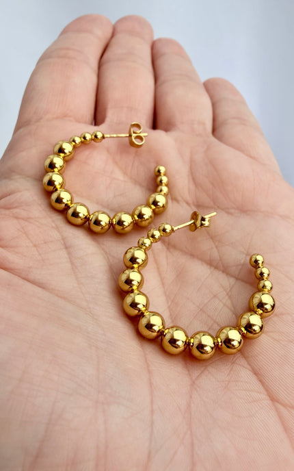 Beaded gold hoop earrings held in hand showing scale, textured beaded design, and 18k gold PVD finish