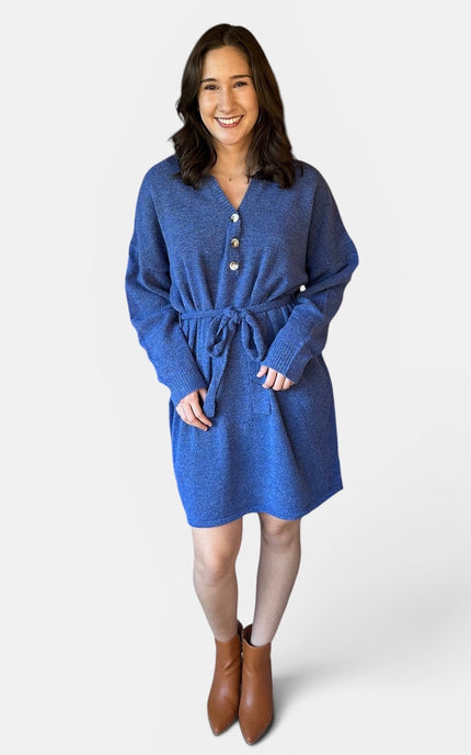 A woman modeling a blue textured knit belted sweater dress with a buttoned neckline, photographed against a light gray studio background.