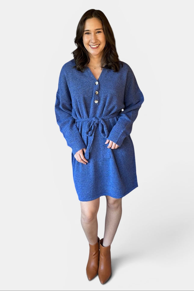 A woman modeling a blue textured knit belted sweater dress with a buttoned neckline, photographed against a light gray studio background.