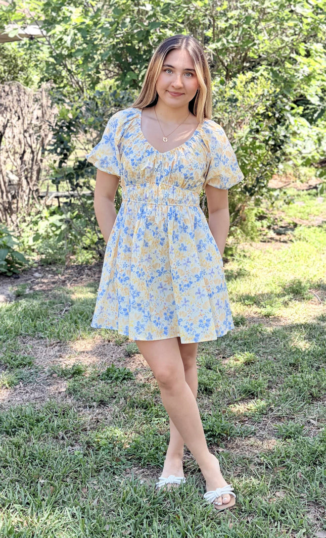 Woman wearing Bloom Bubble Sleeve Dress in watercolor floral print with side pockets, styled casually with sandals for spring