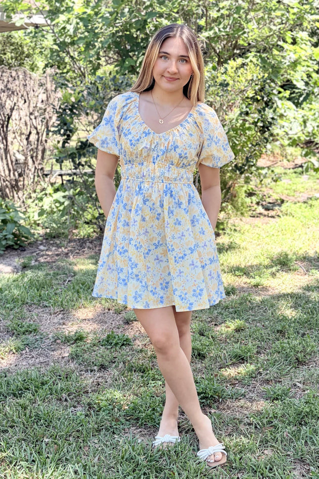 Woman wearing Bloom Bubble Sleeve Dress in watercolor floral print with side pockets, styled casually with sandals for spring