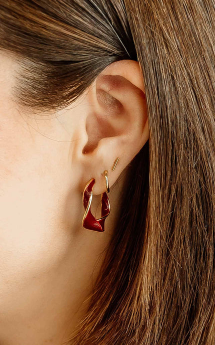 Burgundy and gold twisted 22 mm hoop earrings with gold-plated stainless steel posts, styled on soft linen background
