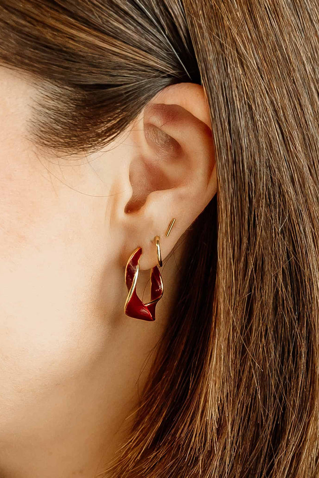 Burgundy and gold twisted 22 mm hoop earrings with gold-plated stainless steel posts, styled on soft linen background