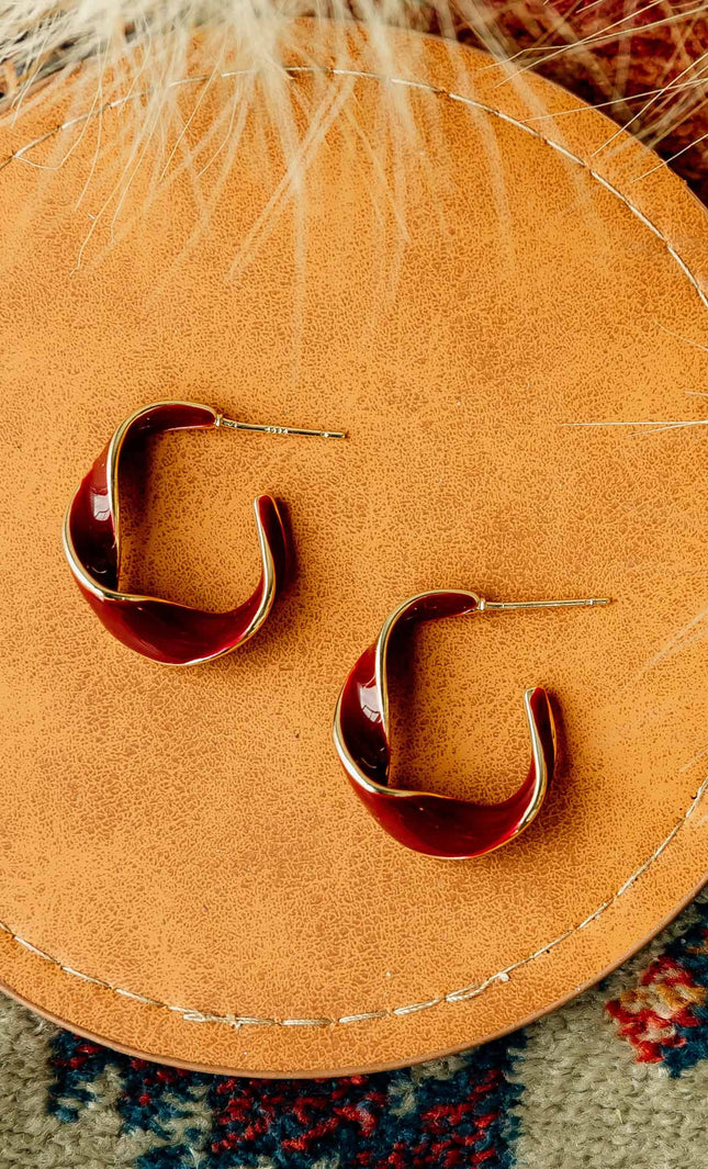 Burgundy and gold twisted 22 mm hoop earrings with gold-plated stainless steel posts, styled on soft linen background