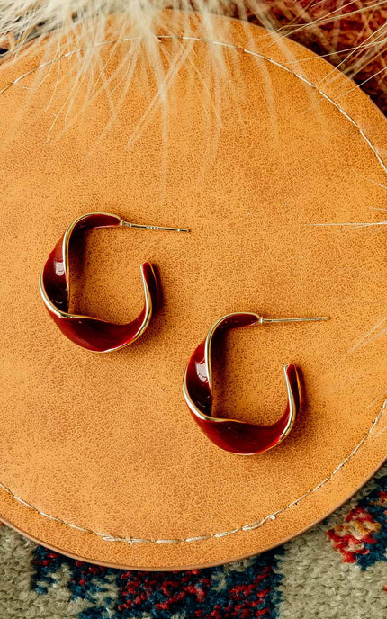 Burgundy and gold twisted 22 mm hoop earrings with gold-plated stainless steel posts, styled on soft linen background