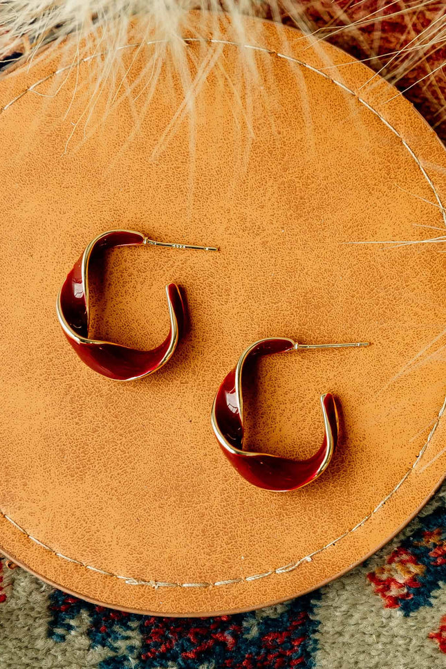 Burgundy and gold twisted 22 mm hoop earrings with gold-plated stainless steel posts, styled on soft linen background