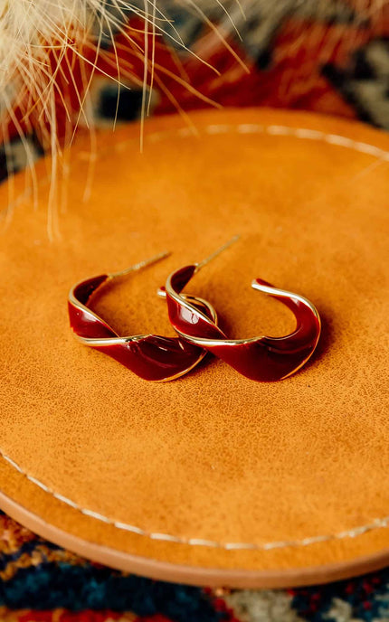 Burgundy and gold twisted 22 mm hoop earrings with gold-plated stainless steel posts, styled on soft linen background