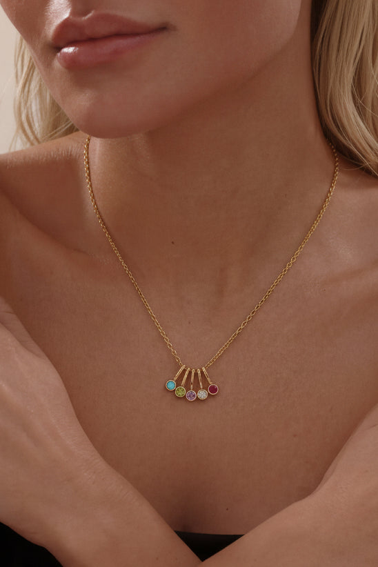 Woman wearing a gold necklace with colorful gemstones against a neutral background