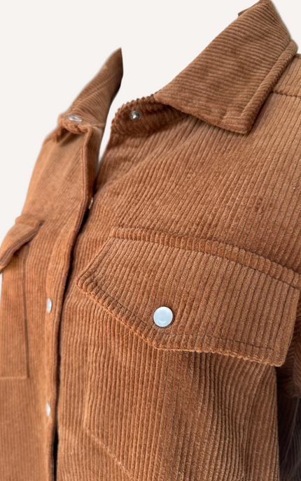 Soft corduroy button-down shacket with a relaxed fit and side pockets, shown in a neutral tone against a clean soft-linen background, styled as a cozy layering piece.