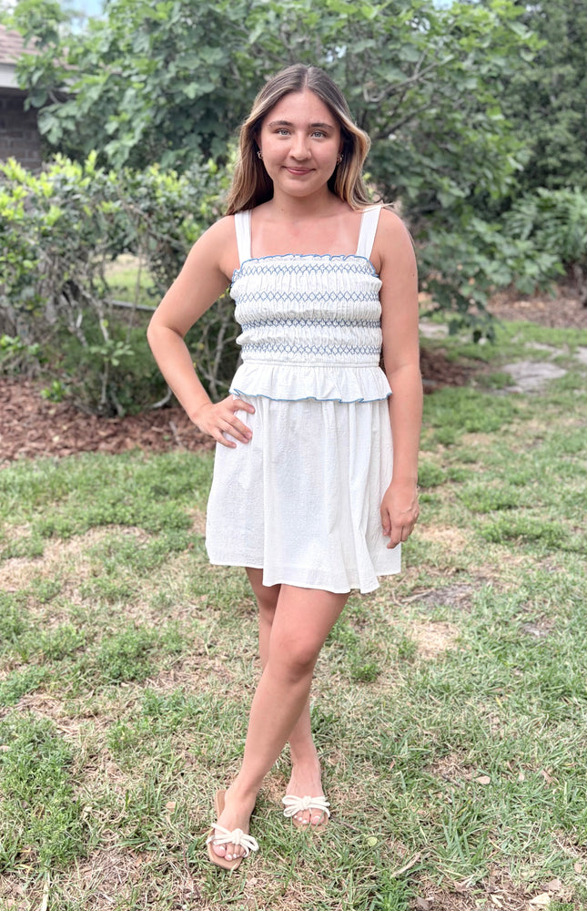 Front view of a feminine romantic white cotton smocked mini dress with a square neckline and flared skirt on a model.