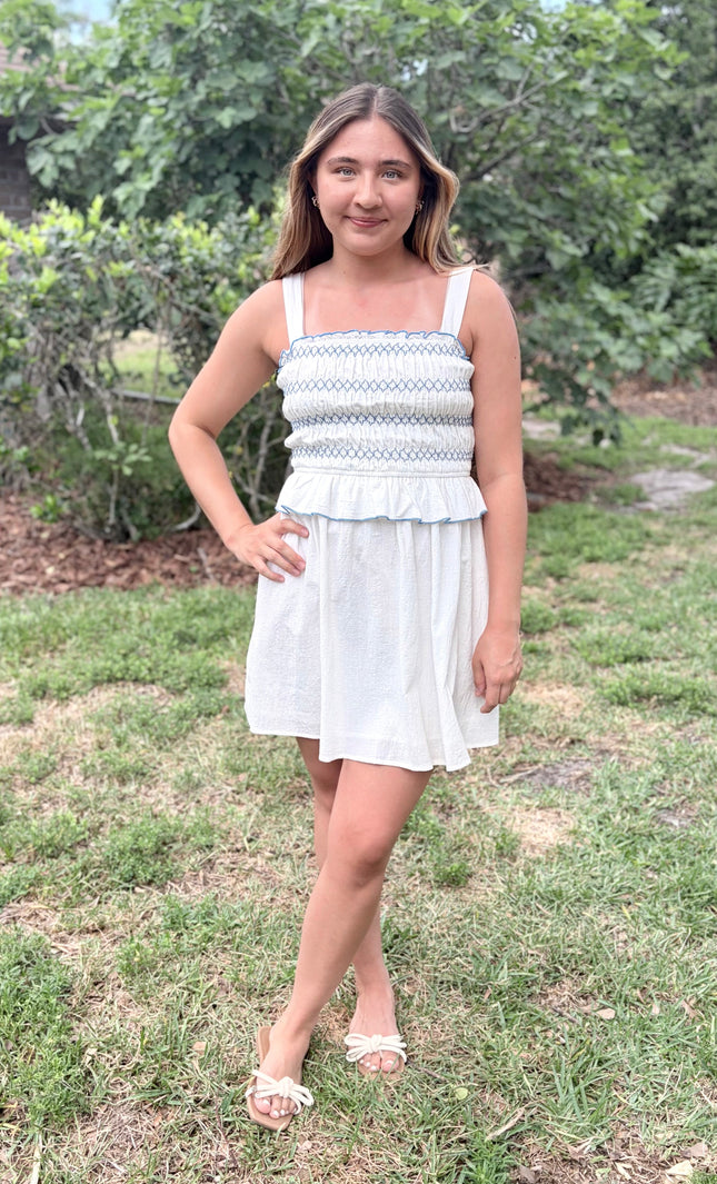 Front view of a feminine romantic white cotton smocked mini dress with a square neckline and flared skirt on a model.