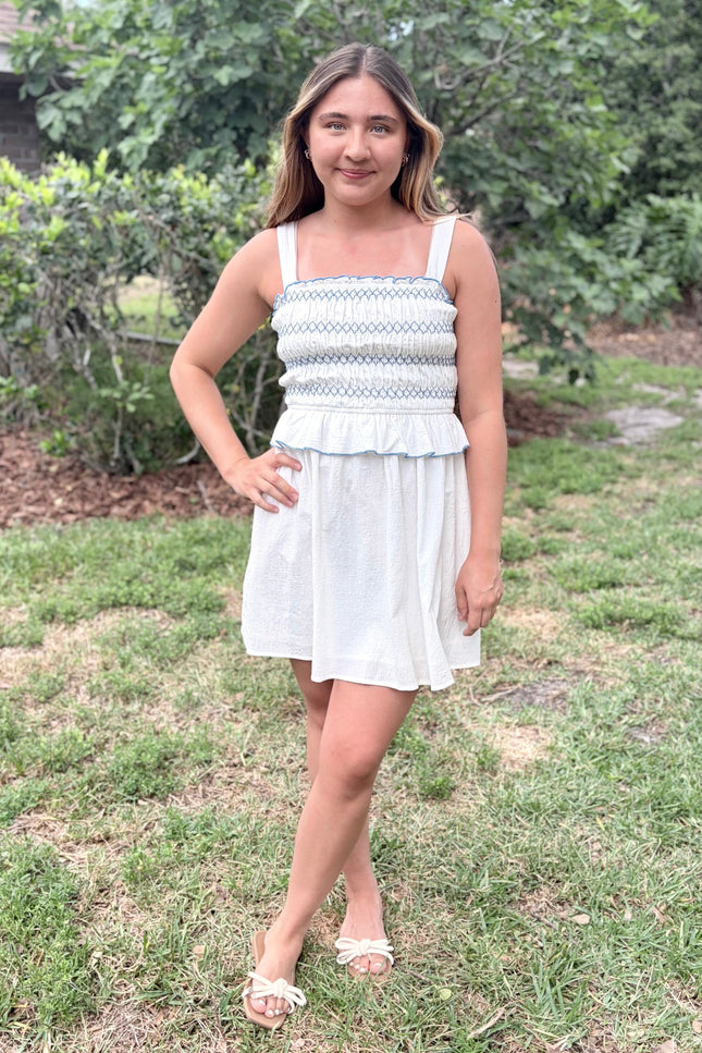 Front view of a feminine romantic white cotton smocked mini dress with a square neckline and flared skirt on a model.
