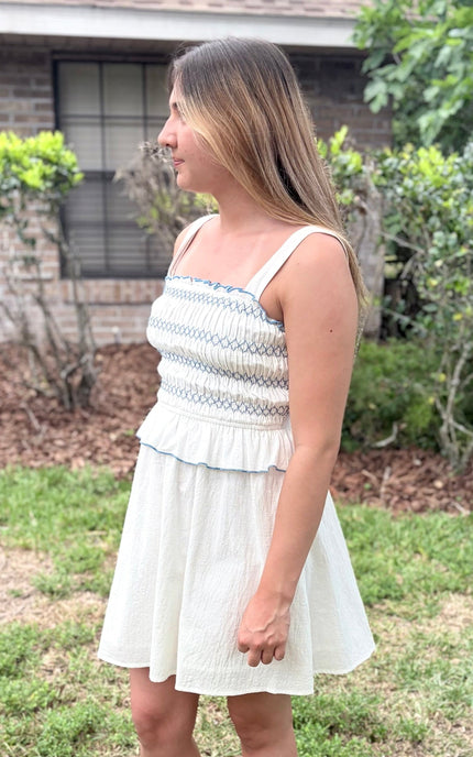 Side view of a feminine romantic white cotton smocked mini dress with a square neckline and flared skirt on a model.