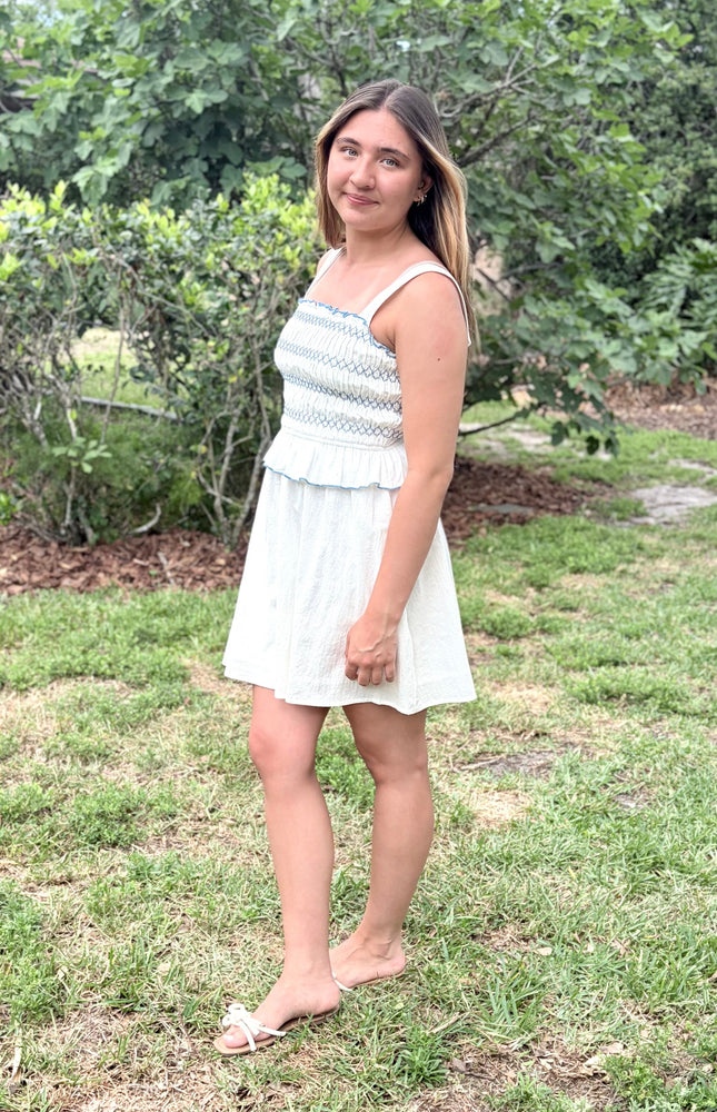 Side view of a feminine romantic white cotton smocked mini dress with a square neckline and flared skirt on a model.