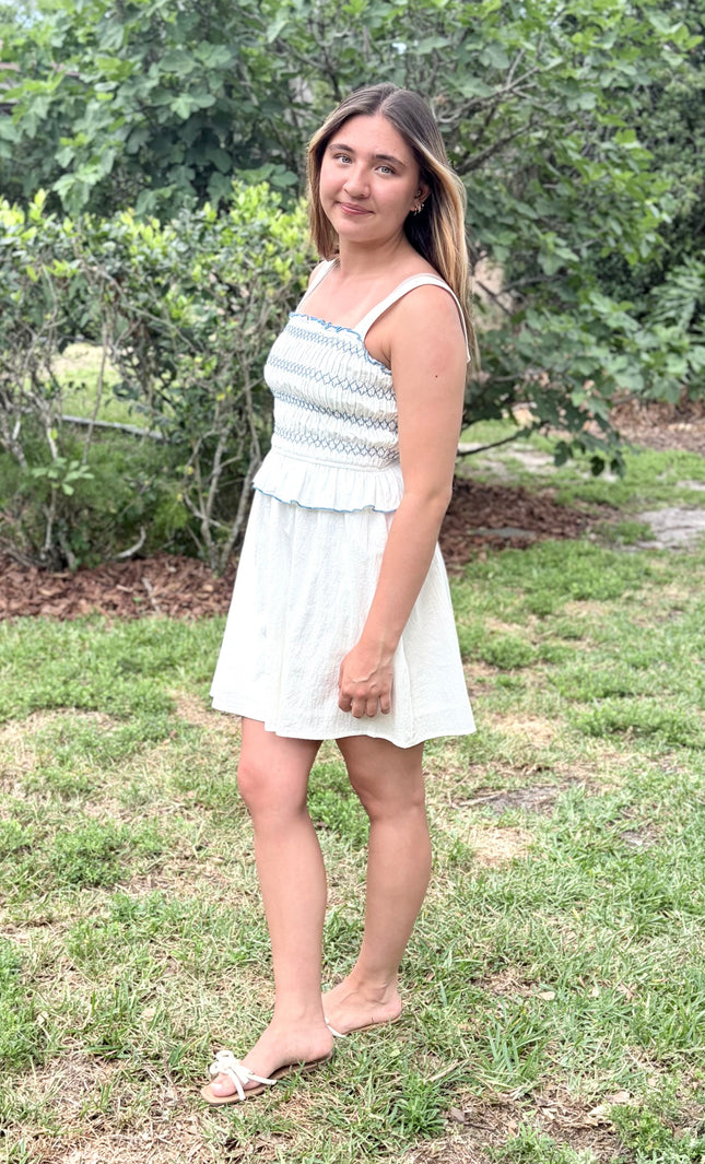 Side view of a feminine romantic white cotton smocked mini dress with a square neckline and flared skirt on a model.