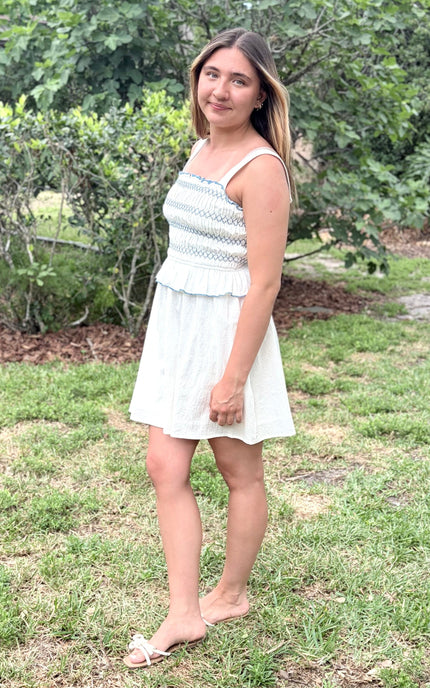 Side view of a feminine romantic white cotton smocked mini dress with a square neckline and flared skirt on a model.