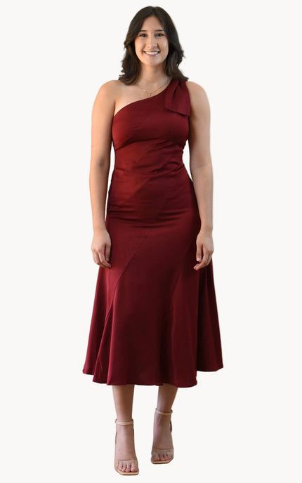 Cranberry Grace Dress with one-shoulder bow detail, slanted seamwork, and flared midi hem, designed for elegant movement, photographed on Soft Linen background.