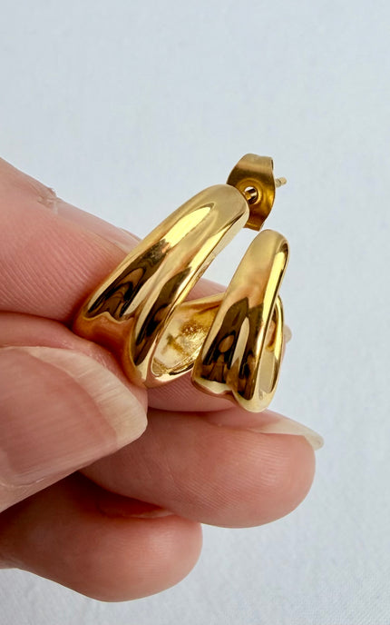 Close-up of hand holding double twist gold hoop earrings showing modern sculpted design and lightweight construction