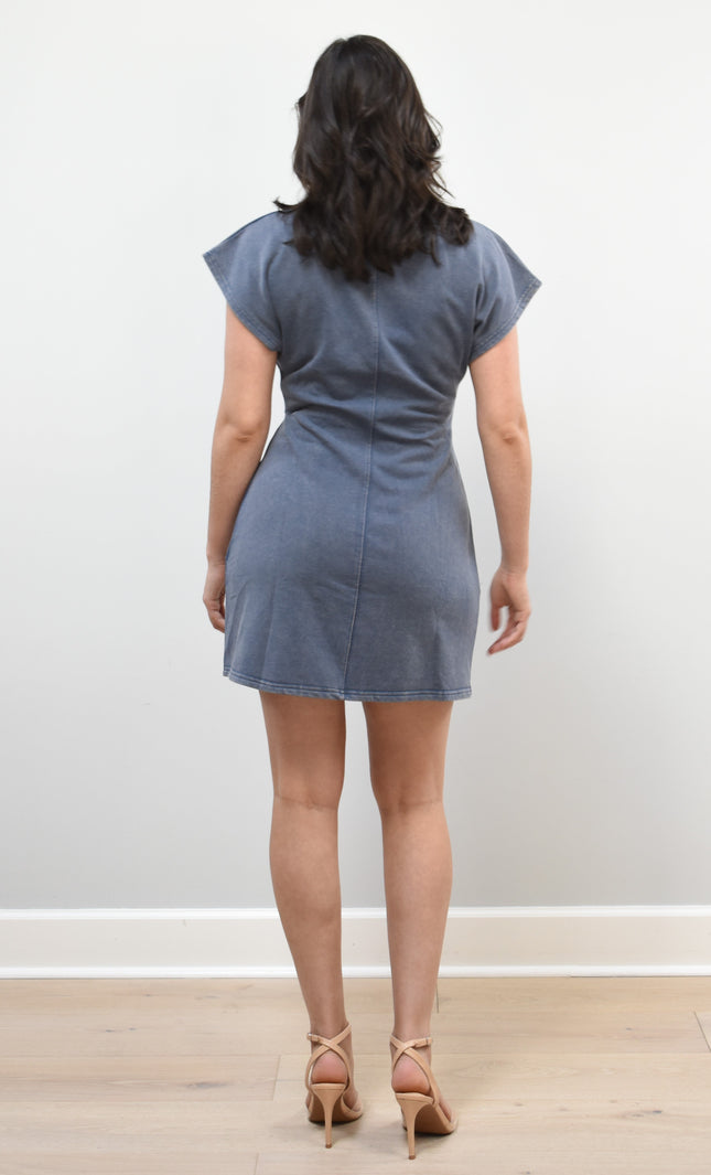 Woman wearing a blue dress standing against a white wall.