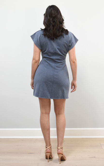 Woman wearing a blue dress standing against a white wall.