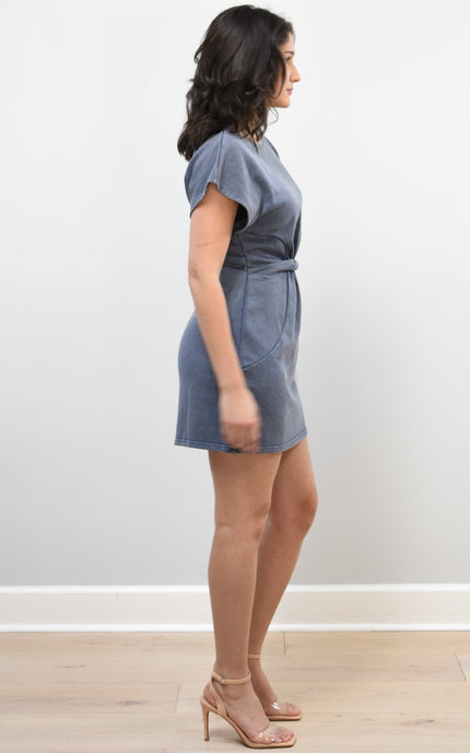 Woman wearing a blue dress standing against a white wall.