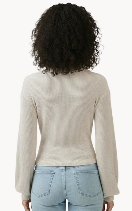 Person wearing a beige sweater and light blue jeans on a white background