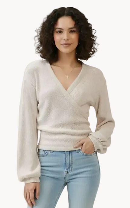 Woman wearing a beige sweater and light blue jeans on a plain background