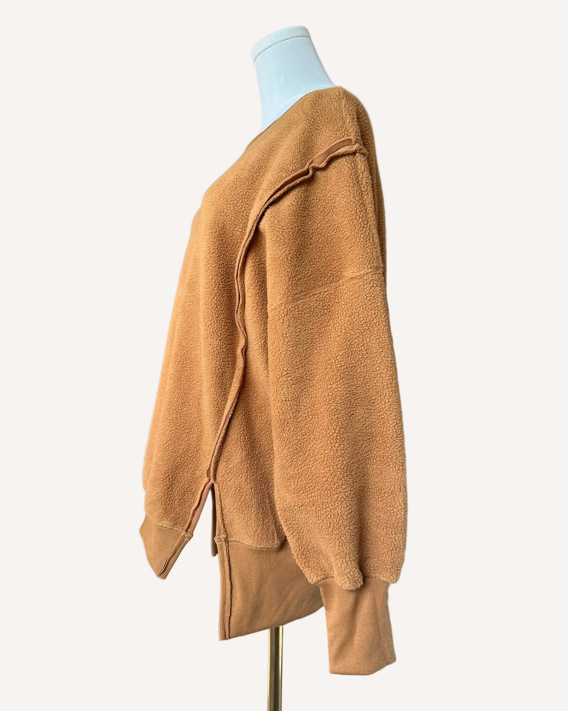 Soft fleece pullover with a relaxed fit, dropped shoulders, and reverse seam detailing, shown in a neutral tone against a clean soft-linen background.
