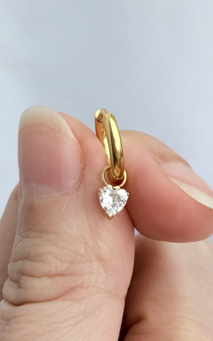 Gold hoop earrings with heart crystal drop held in hand showing scale, sparkle detail, and 18k gold PVD finish